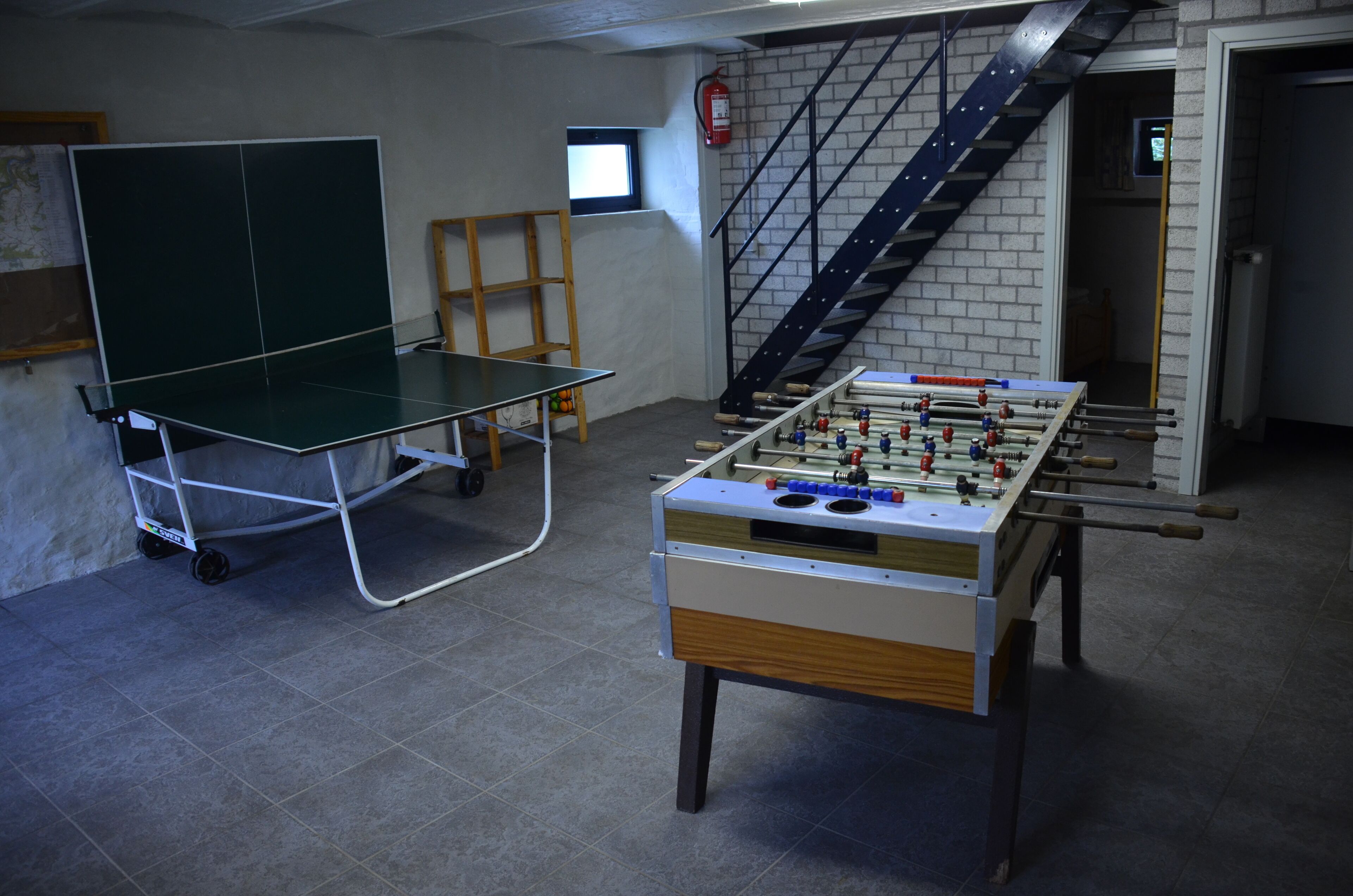 A room with a foosball table, a ping pong table, and a staircase.