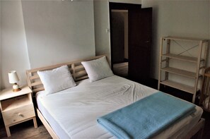 Une chambre à coucher avec un lit en bois, du linge de lit blanc, une table de chevet avec une lampe et une couverture bleue.
