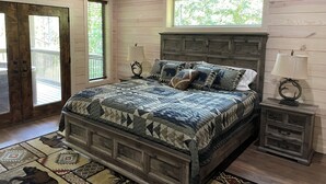 A bedroom with a wooden bed, a nightstand, a ceiling fan, and a window with a view of trees.