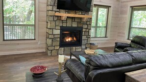 A cozy living room with a stone fireplace, leather sofa, and a flat-screen TV mounted on the wall.