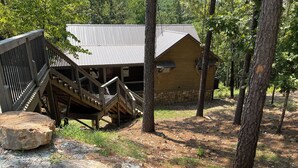 A rustic cabin with a metal roof, wooden stairs, and a stone foundation.