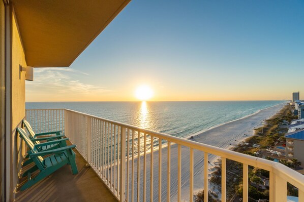 A balcony with a view of the ocean and beach at sunset.