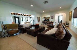 A spacious living room with a large brown leather sofa, a wooden coffee table, and a floor lamp. There is a kitchen visible in the background. - Casa by the Sea Pompano Beach (Pompano Beach)