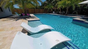 Une piscine avec deux chaises longues blanches et des palmiers en arrière-plan.
