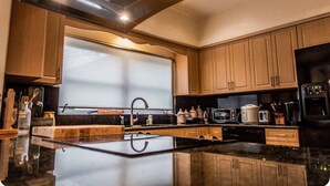 Une cuisine moderne avec des meubles en bois, un plan de travail noir et divers appareils, notamment un four à micro-ondes et une machine à café.