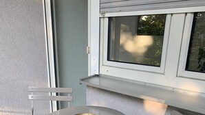 A small outdoor seating area with a round table and two chairs, a window above, and artificial grass. - Apartments Mitte Messe und Zentrum (Nürnberg)