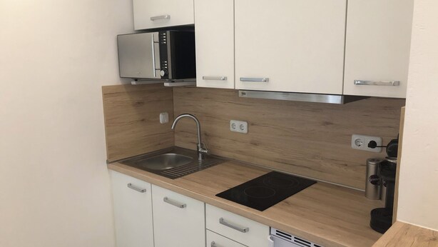 A compact kitchen with white cabinets, a stainless steel sink, a microwave, and a built-in stove. - Apartments Mitte Messe und Zentrum (Nürnberg)