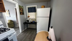 A compact kitchen with a stove, microwave, refrigerator, and a small dining table.