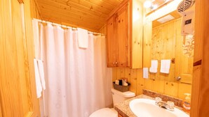 Een houten badkamer in cottage-stijl met douchegordijn, toilet, wastafel en houten kastjes.