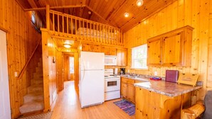 Een houten chalet van binnen, met een keuken, een eethoek en een trap naar een slaapzolder.