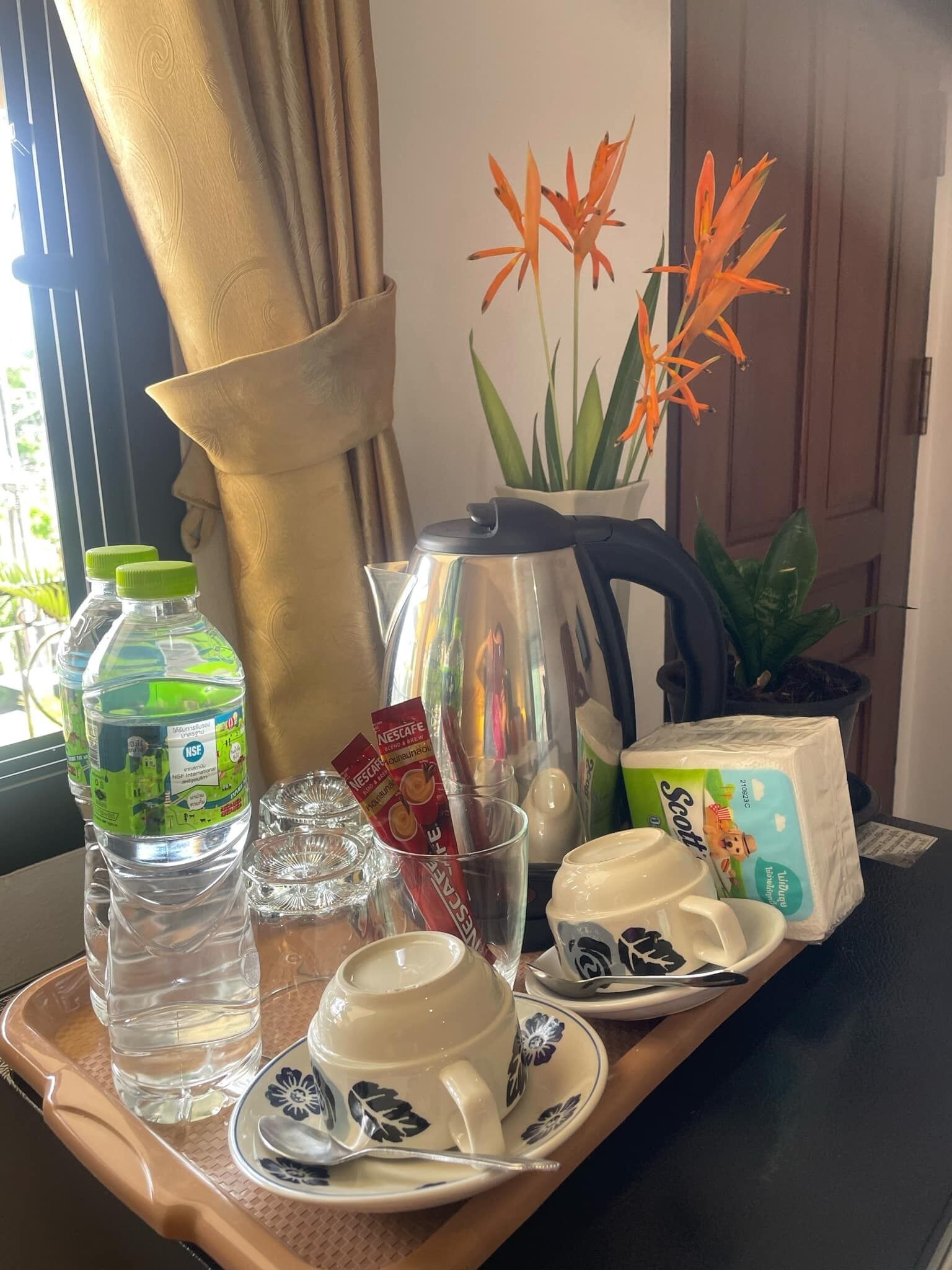 Una bandeja con una botella de agua, una cápsula de café Nescafé, un vaso, una tetera, una caja de pañuelos Scott y un juego de tazas y platillos blancos.