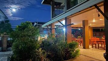 A restaurant with outdoor seating, a balcony, and a well-lit entrance.