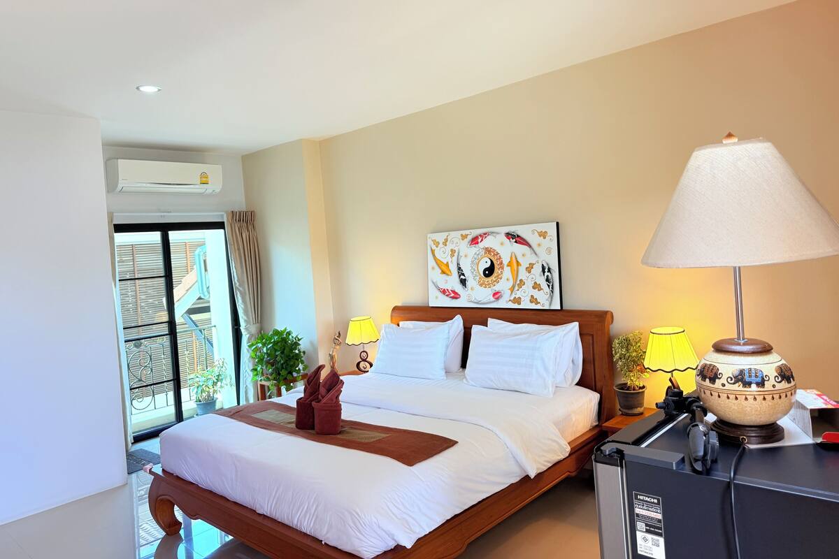 A hotel room with a bed, a bedside lamp, a painting, and a view of the outside balcony.