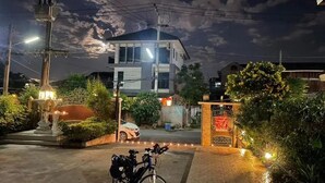 A residential area at night with a well-lit entrance, a parked bicycle, and a car in the background. - Laph Kham House (Chiang Mai)