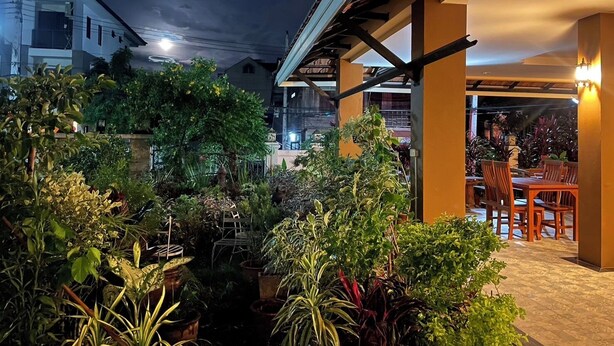 An outdoor patio area with a dining table and chairs, surrounded by potted plants and a pergola structure. - Laph Kham House (Chiang Mai)