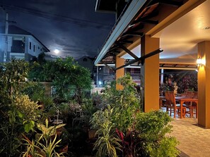 An outdoor patio area with a dining table and chairs, surrounded by potted plants and a pergola structure. - Laph Kham House (Chiang Mai)