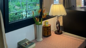 A hotel room with a large window, a bedside lamp, a vase with flowers, and a bedside table with a book and a telephone. - Laph Kham House (Chiang Mai)