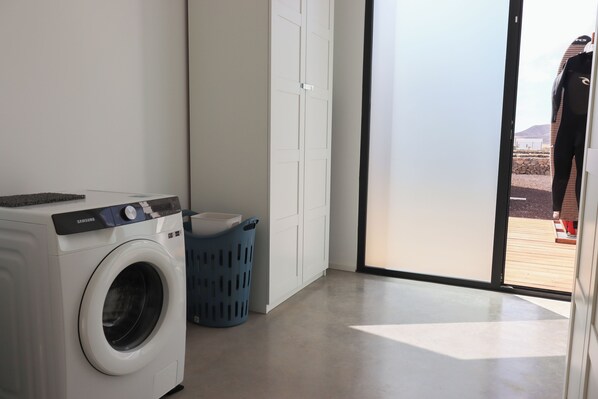 A laundry area with a washing machine, a blue laundry basket, and a door leading to an outdoor area.