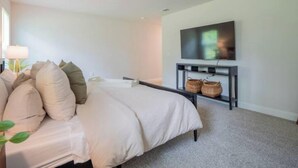 Een slaapkamer met een bed, een aan de muur bevestigde televisie en een klein console tafeltje met manden.