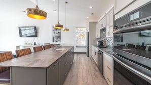Una cocina moderna con una isla grande, electrodomésticos de acero inoxidable e iluminación colgante.