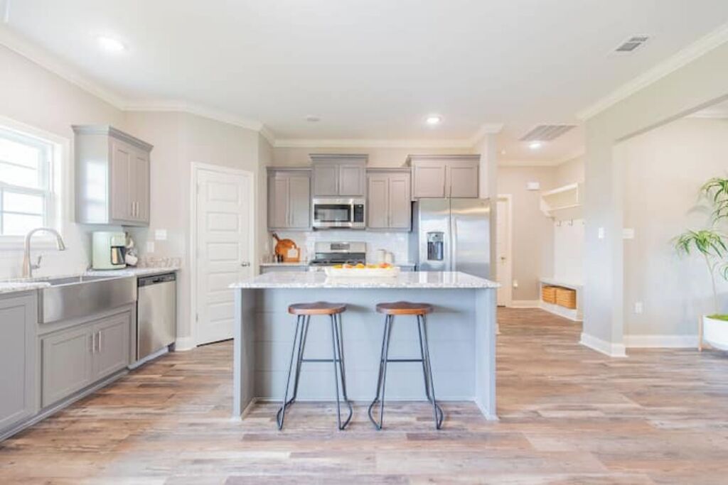 A modern kitchen with grey cabinets, stainless steel appliances, and a central island with stools.