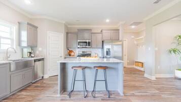 A modern kitchen with grey cabinets, stainless steel appliances, and a central island with stools.