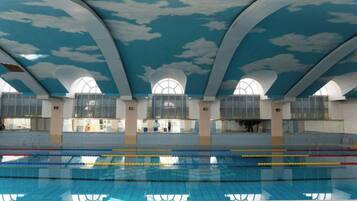 An indoor swimming pool with a high ceiling and arched windows.