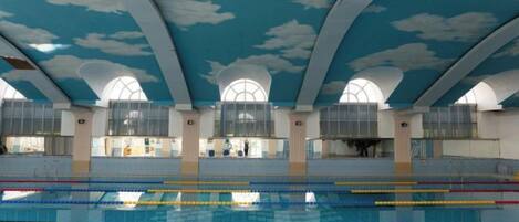 An indoor swimming pool with a high ceiling and arched windows.