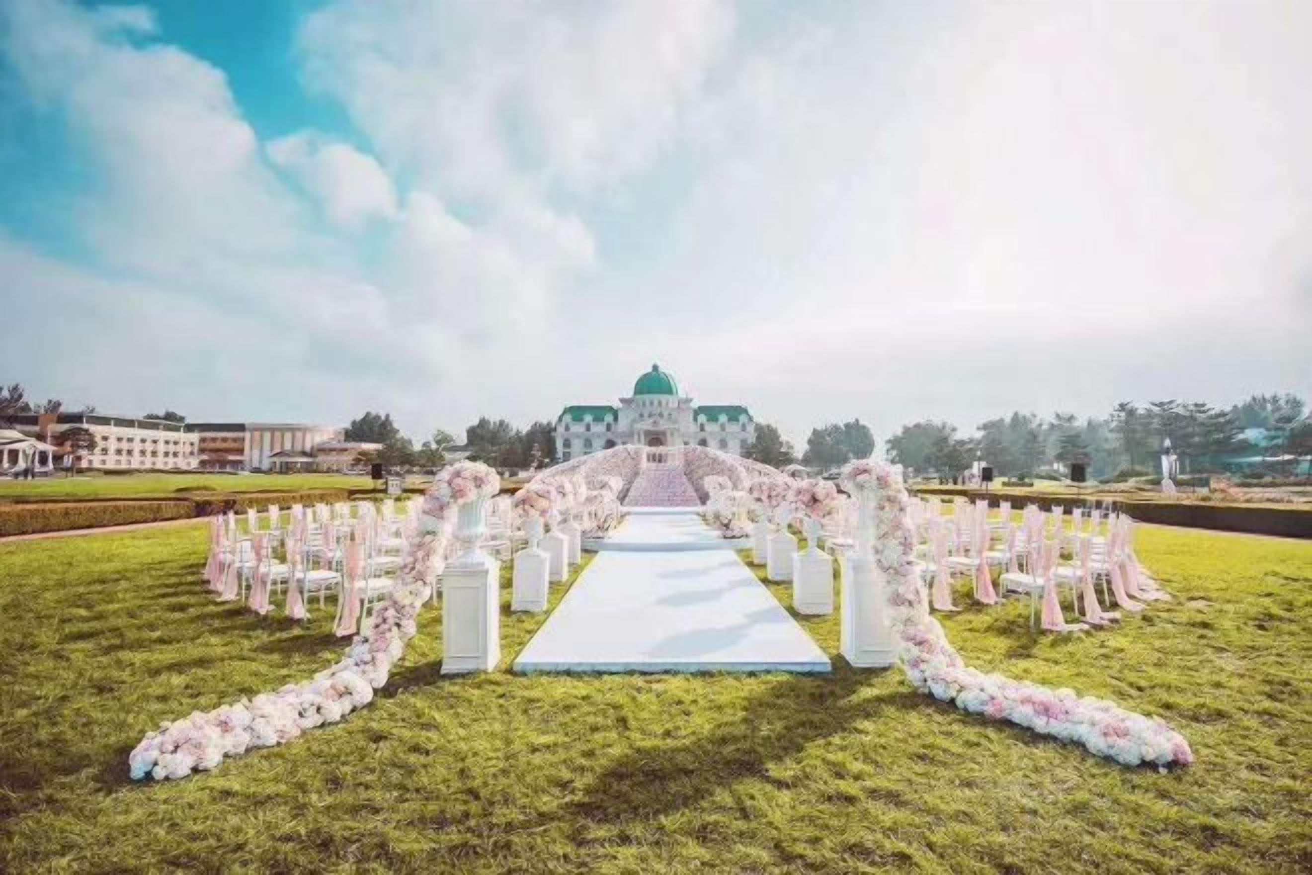 Un lugar para bodas al aire libre con un pasillo blanco y arreglos florales.