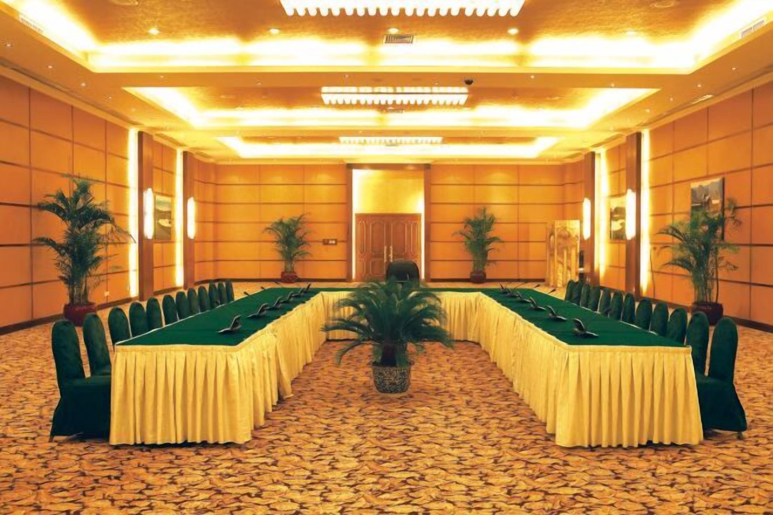 Un salón de conferencias con una larga mesa, sillas y plantas en macetas.