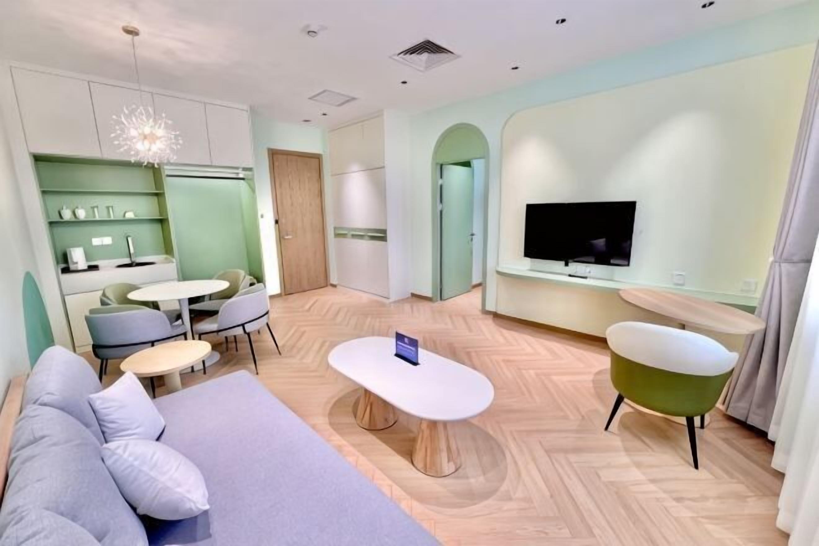 A modern living room with a sofa, a dining table, a TV, and a kitchen area.