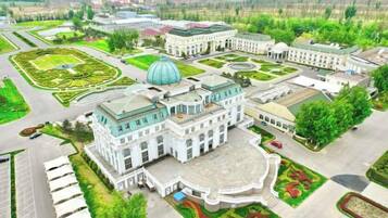 A large, historic building with a central dome, surrounded by manicured gardens and multiple wings.