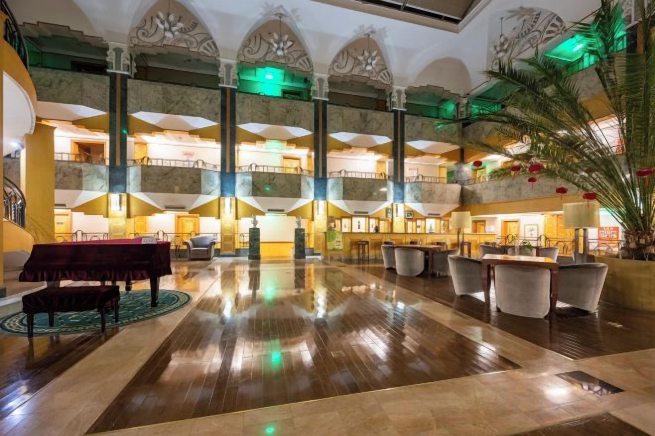 A spacious lobby with a grand piano, multiple seating areas, and a high ceiling with decorative elements.