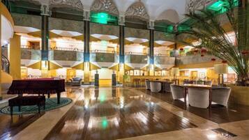 A spacious lobby with a grand piano, multiple seating areas, and a high ceiling with decorative elements.