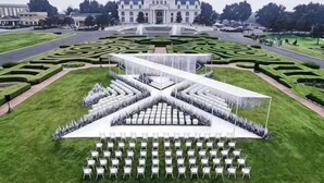 A formal outdoor event setup with a tent, chairs, and a fountain in a well-manicured garden with a large building in the background. - Reignwood Pine Valley (Beijing)