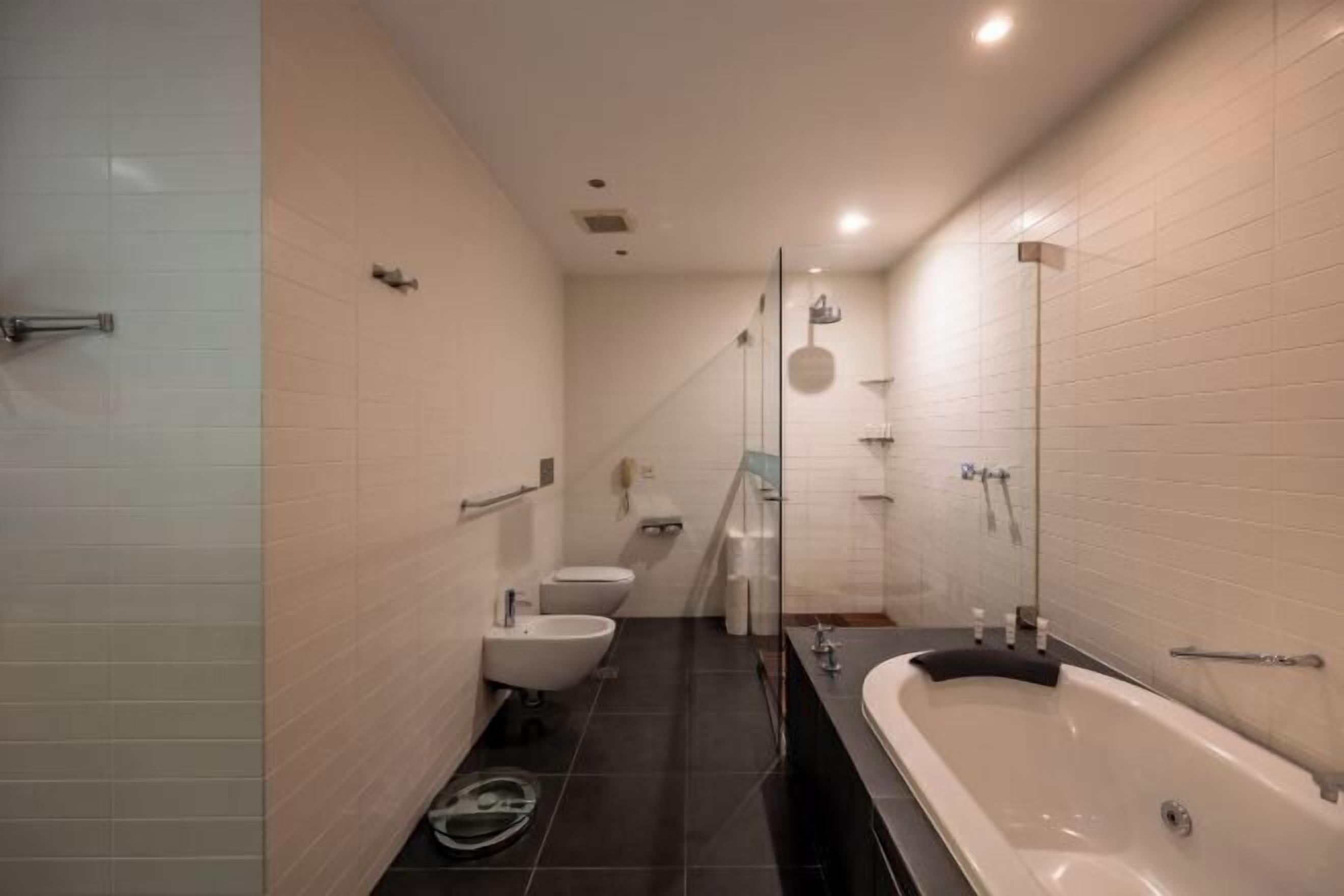 Uma casa de banho moderna com banheira, dois sanitários e um bidé.