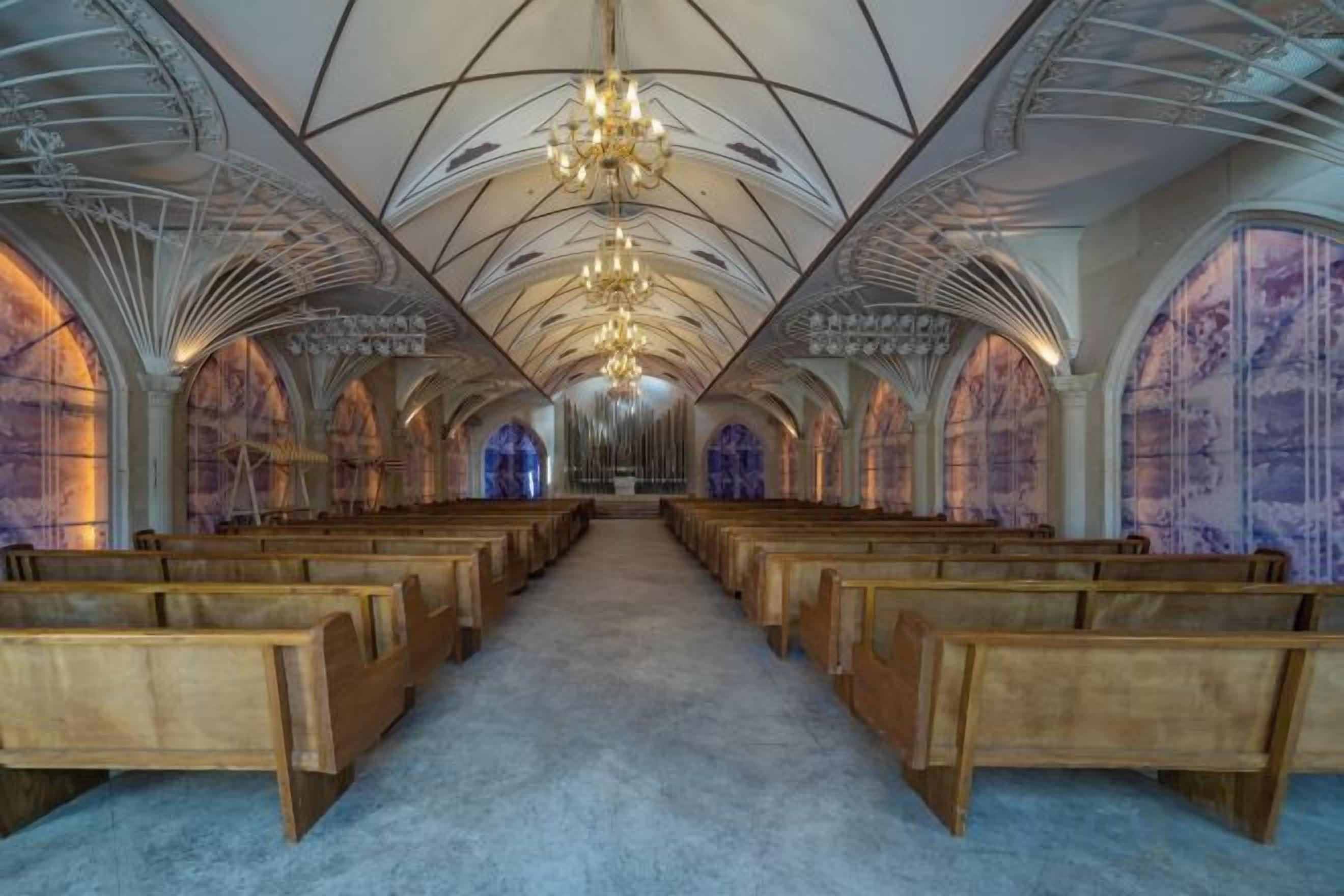 An interior with rows of wooden pews, a high arched ceiling, and a central aisle leading to a focal point.
