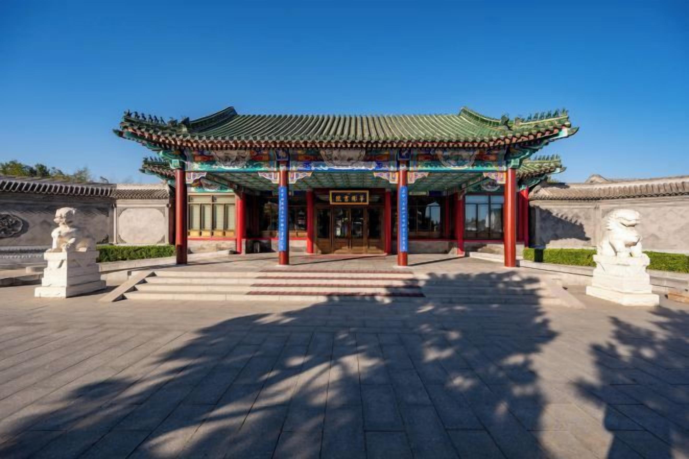 Um pavilhão chinês tradicional com telhado de azulejos, entrada de pedra e duas estátuas de leões de cada lado.