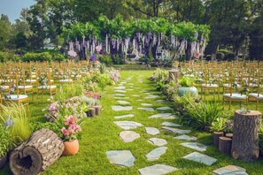 An outdoor wedding venue with a stone pathway, chairs arranged in rows, and hanging floral decorations. - Reignwood Pine Valley (Beijing)