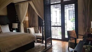 A bedroom with a large bed, a chair, a desk, and a window with a view of greenery. - Reignwood Pine Valley (Beijing)