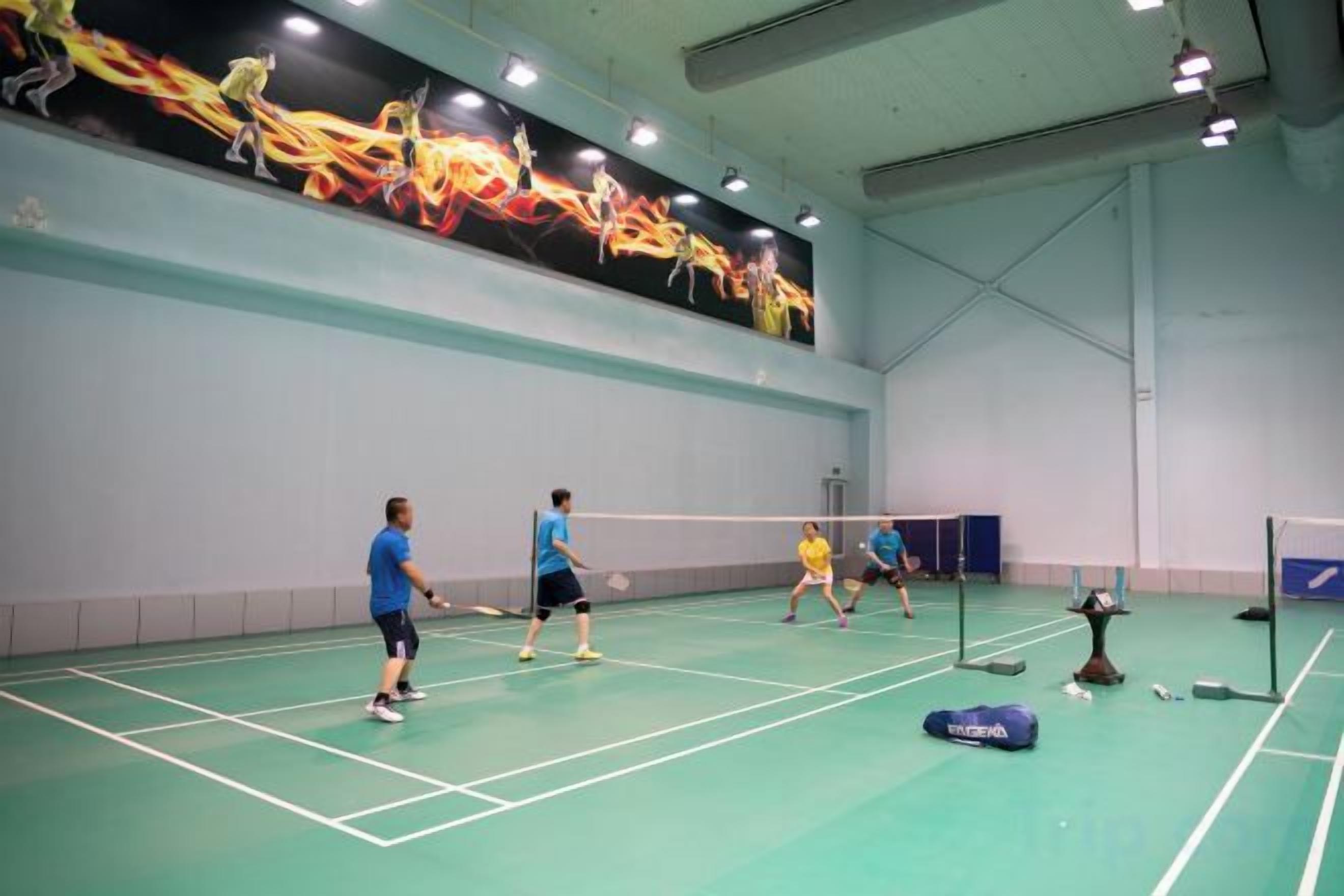 Una cancha de bádminton interior con jugadores, una red y una pared con un mural.