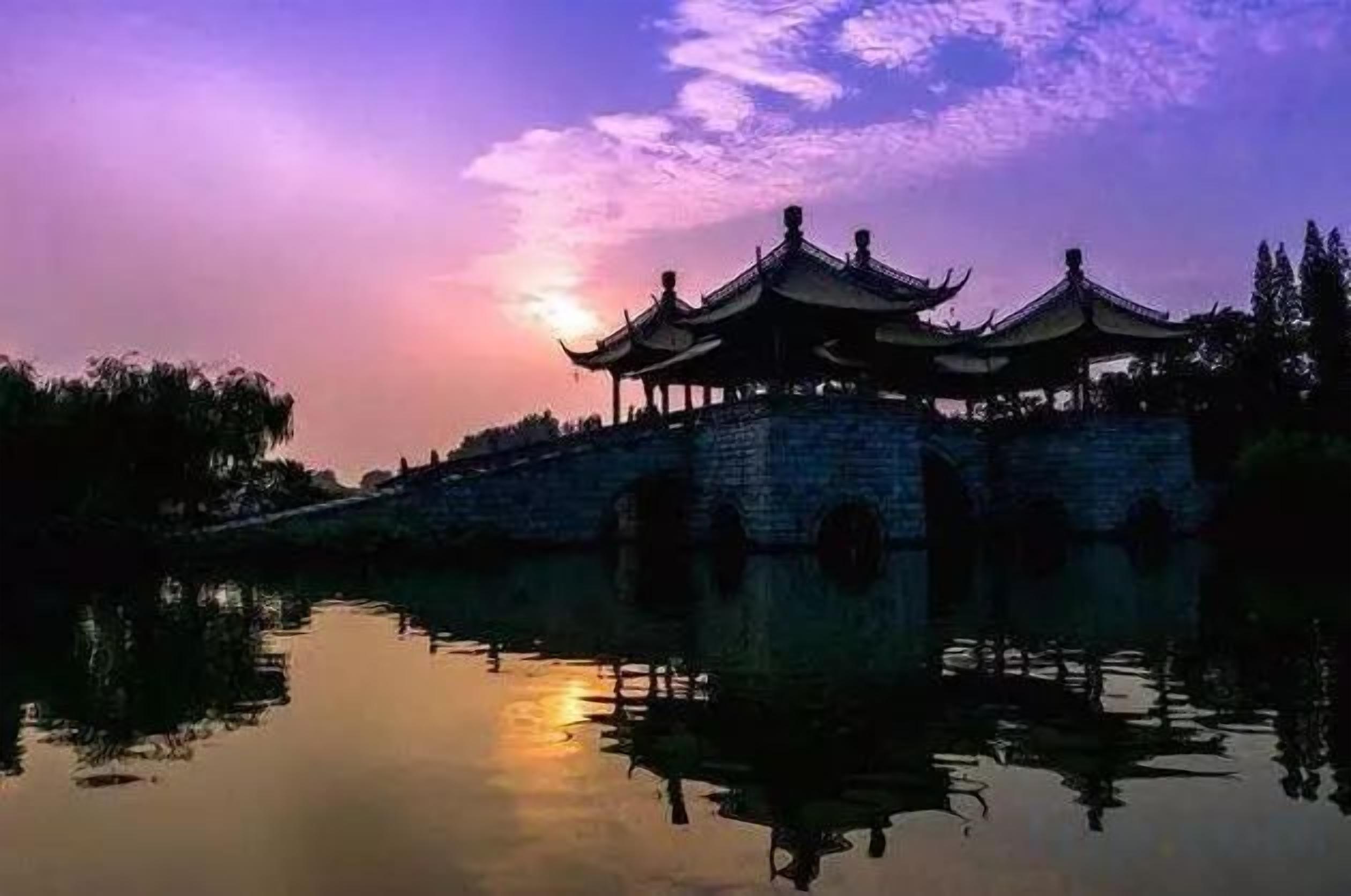 A traditional building with multiple roofs, a stone wall, and a reflection in the water.