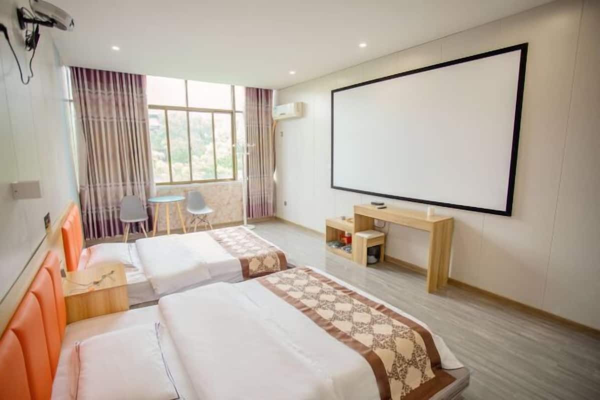 Une chambre d’hôtel avec deux lits, un bureau, une chaise, une grande fenêtre avec des rideaux et un téléviseur fixé au mur.