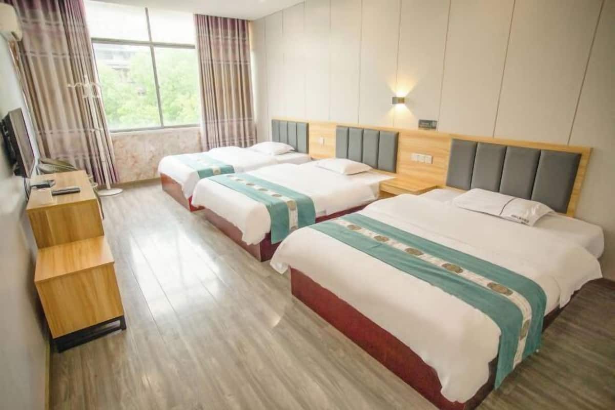 Une chambre d’hôtel avec deux lits, un bureau en bois, une télévision et une fenêtre avec des rideaux.