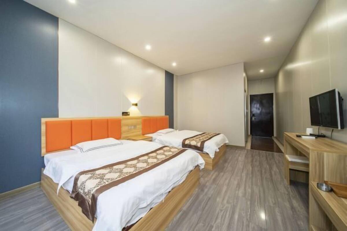 Une chambre d’hôtel avec deux lits, un bureau, une télévision et une lampe fixée au mur.