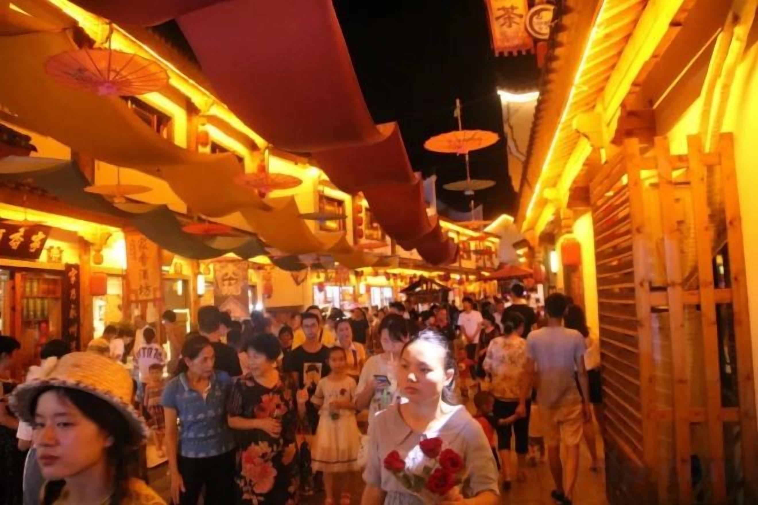A crowded indoor walkway with people walking, overhead lighting, and traditional architectural elements.