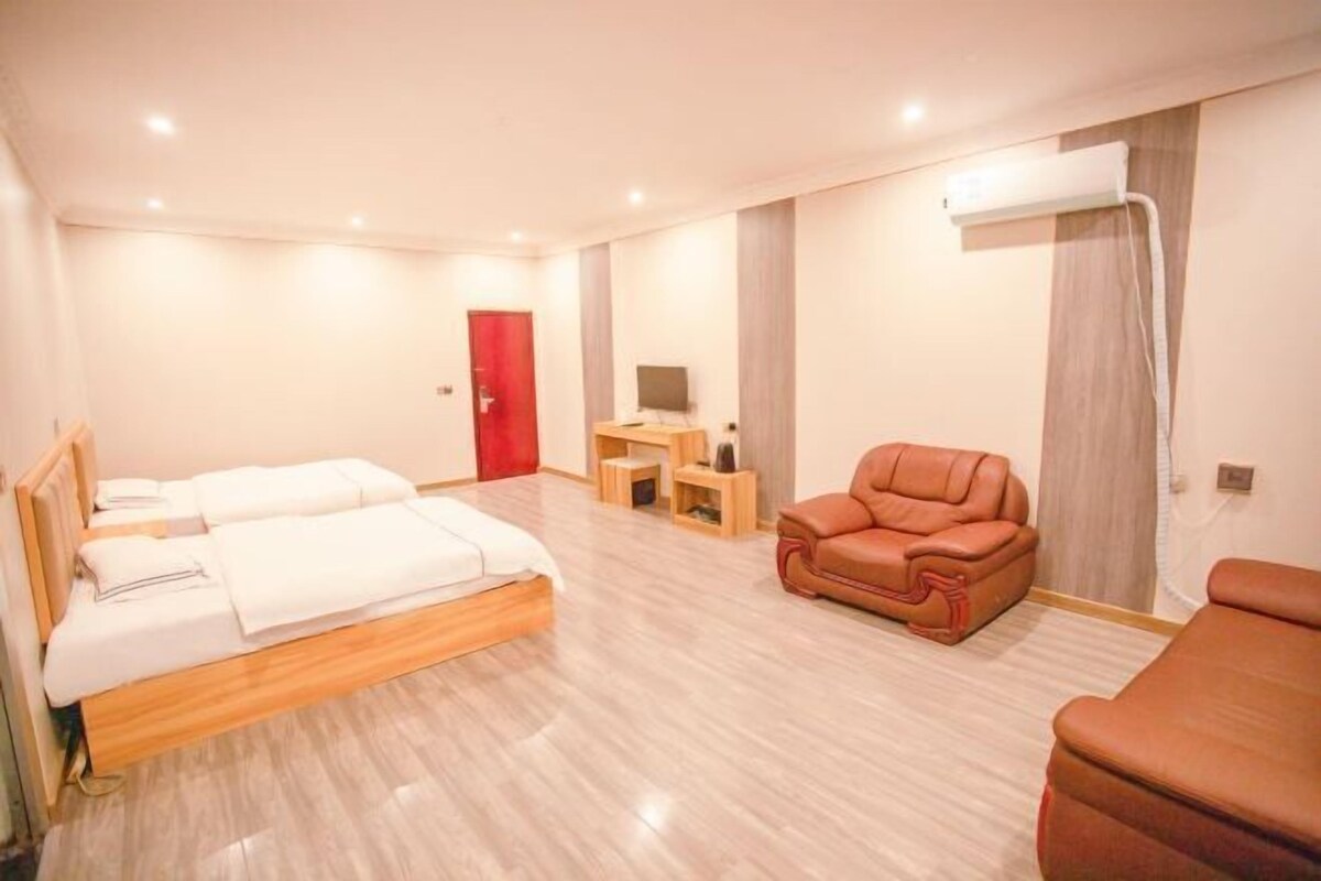 A hotel room with a bed, a sofa, a TV, a desk, and a red door.