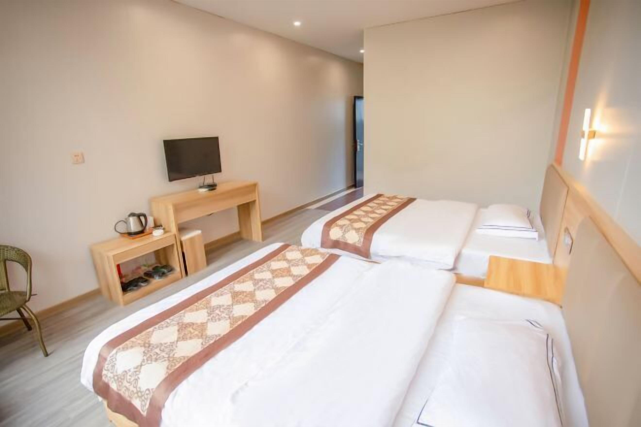 A hotel room with two beds, a TV, a desk with a kettle, and a chair.