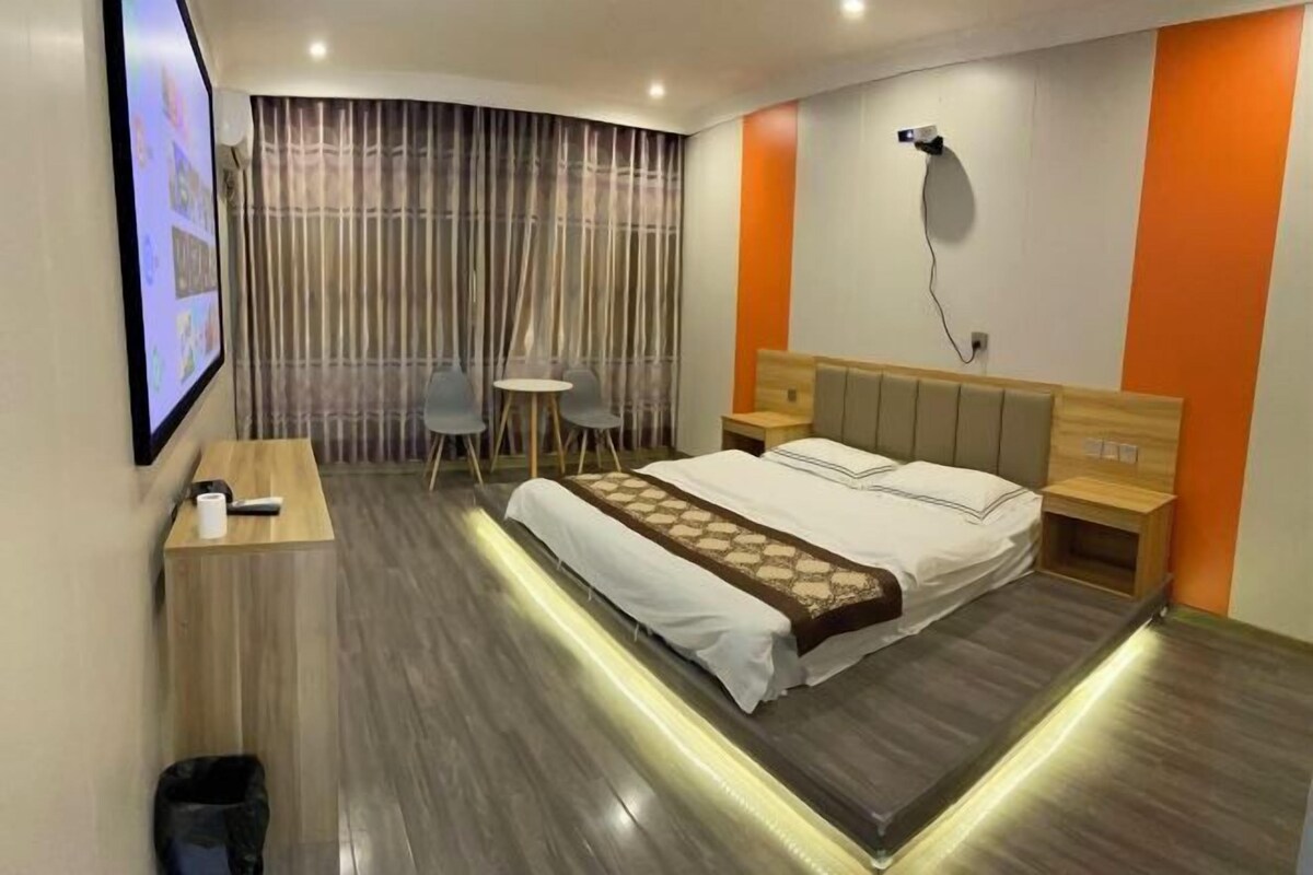 A hotel room with a bed, bedside tables, a desk, a chair, a TV, and a curtain.
