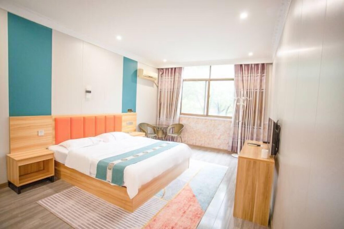 A modern hotel room with a wooden bed, a small desk, a chair, and a TV.
